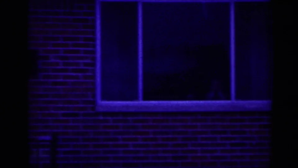 Close 8mm view of a brick building window in New Jersey, tinted blue, with a faint person visible behind the glass.