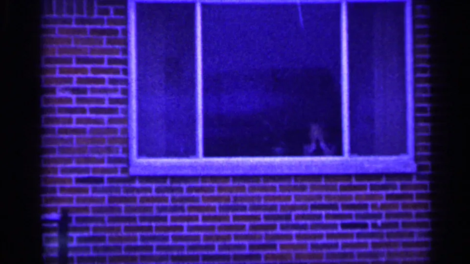 Final frame of a blue-cast brick window, likely in New Jersey, with a faint person visible through the lower glass.