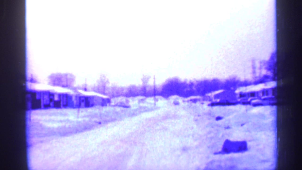 Snow-covered suburban street with small houses and parked cars.