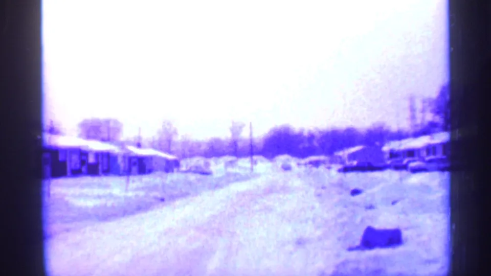 1958 New Jersey home-movie frame showing a snowy suburban street, single-story houses, parked cars, and bare winter trees.
