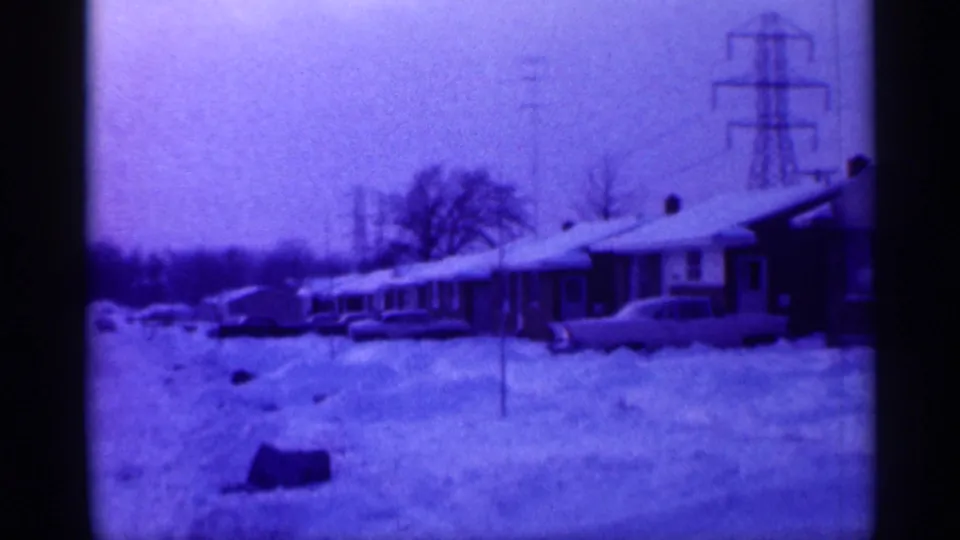 Snow-covered suburban homes in New Jersey, with mid-century cars, utility poles, and transmission towers visible beyond the street.