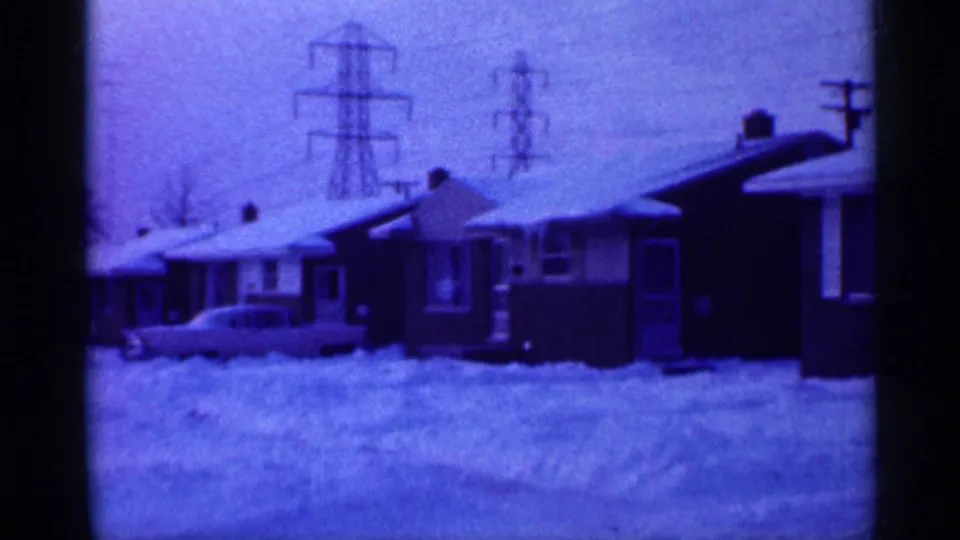 A closer 1958 New Jersey frame shows snow piled around low suburban houses, parked cars, and large transmission towers.