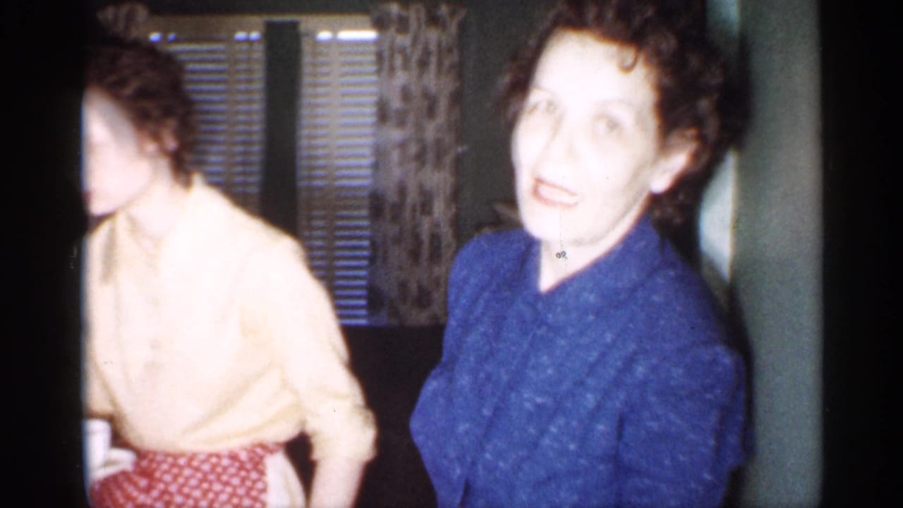 A woman in a blue patterned dress faces the camera in a 1958 New Jersey home interior as another woman in an apron stands nearby.
