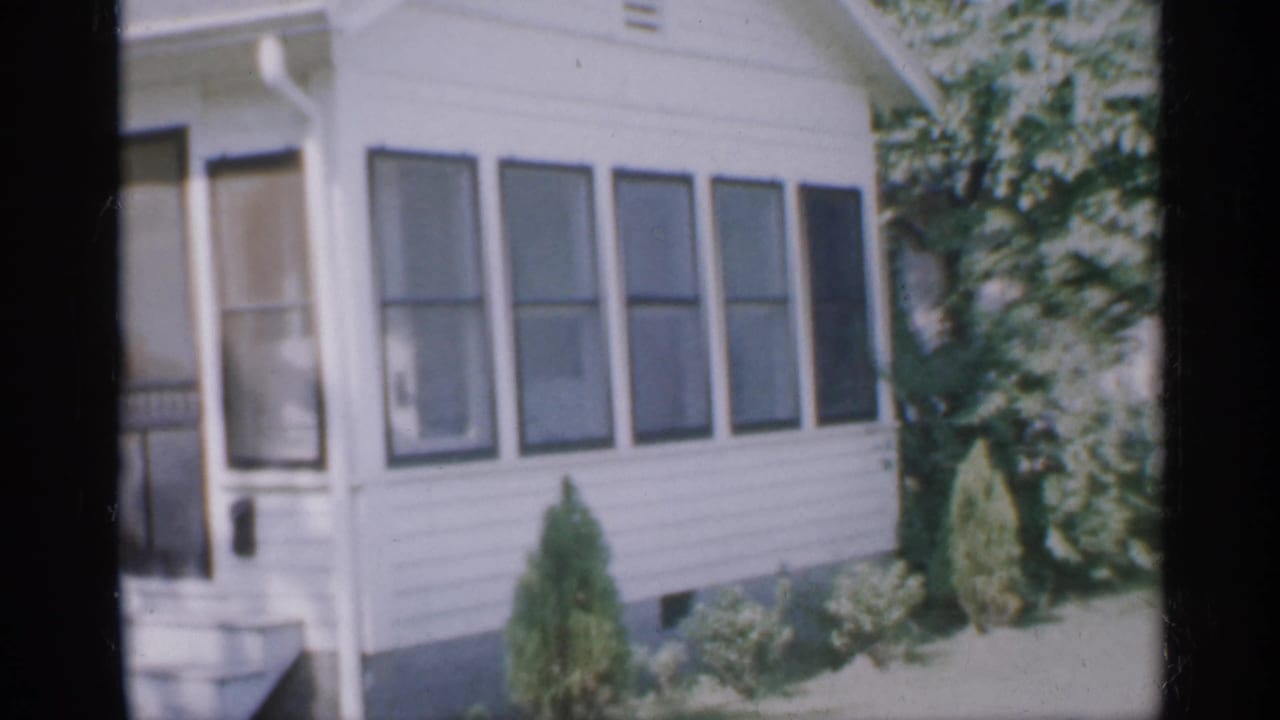 White house exterior with screened porch door, windows, shrubs, and tree canopy.