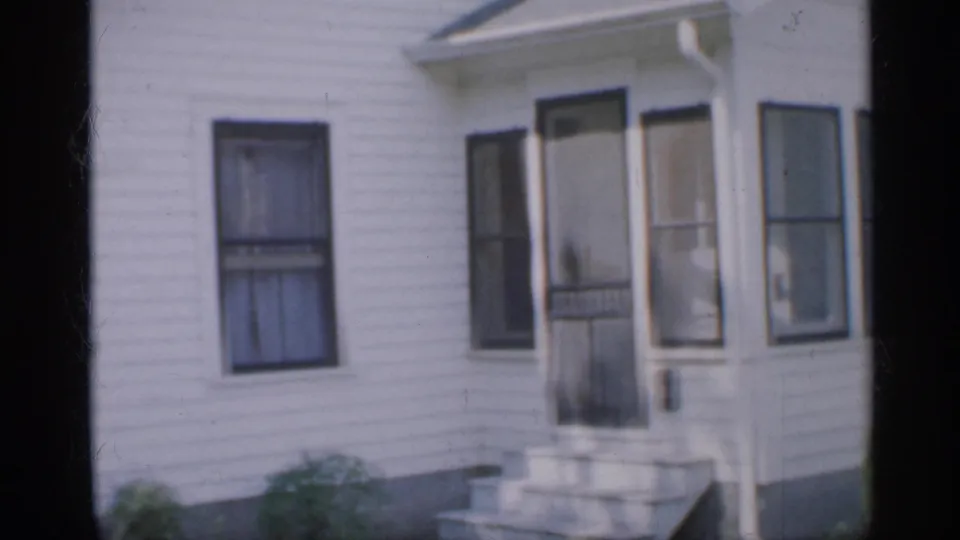 1958 New Jersey frame showing the house entry area with concrete steps, a screened door, adjacent windows, shutters, siding, and low shrubs.