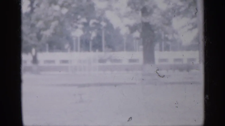 Soft 1958 New Jersey home-movie frame showing an empty park area with trees, pale fencing, and heavy film gate edges.
