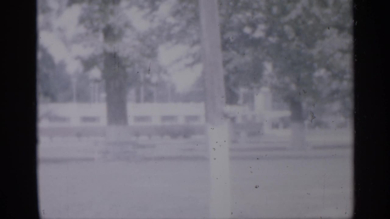 Soft 1958 New Jersey frame of an empty playground or park area bordered by trees and a low pale fence.