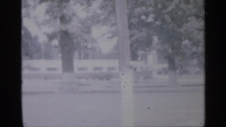 Soft 1958 New Jersey frame of an empty playground or park area bordered by trees and a low pale fence.