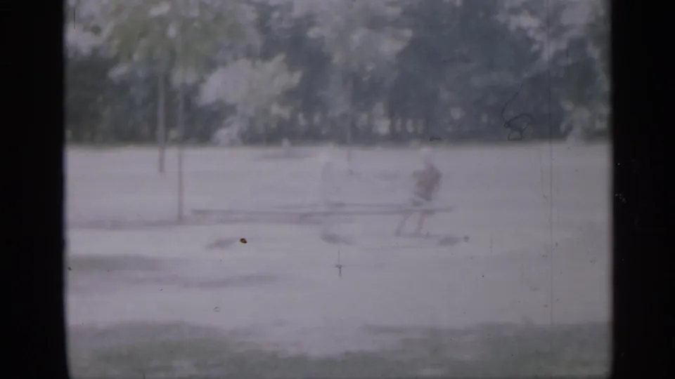 1958 New Jersey home-movie frame with a small child near a low playground structure in an otherwise empty park.