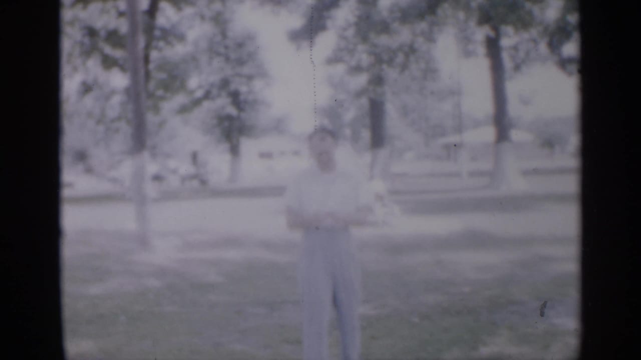 Soft 8mm frame of a man standing on grass among trees.