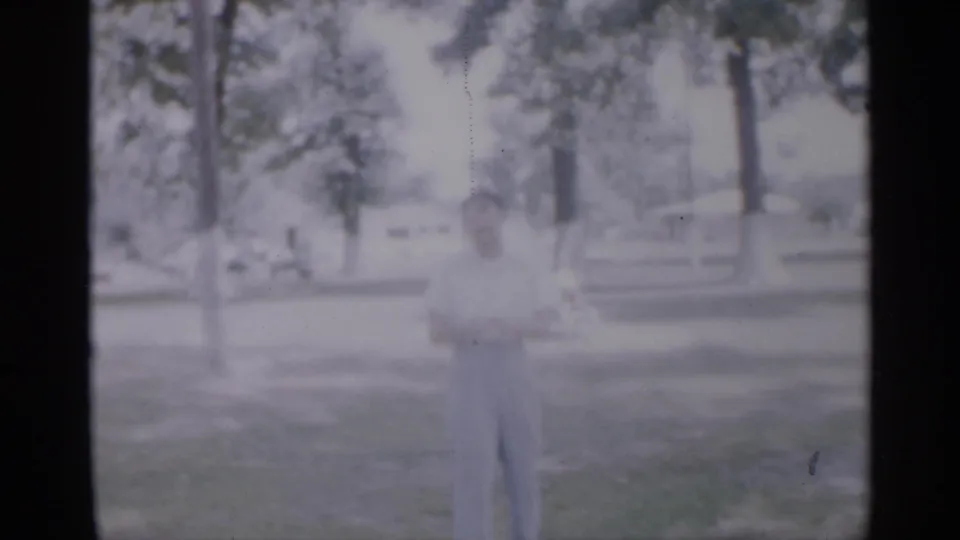 A young man in light clothing stands in a grassy New Jersey park setting in 1958 home-movie footage.