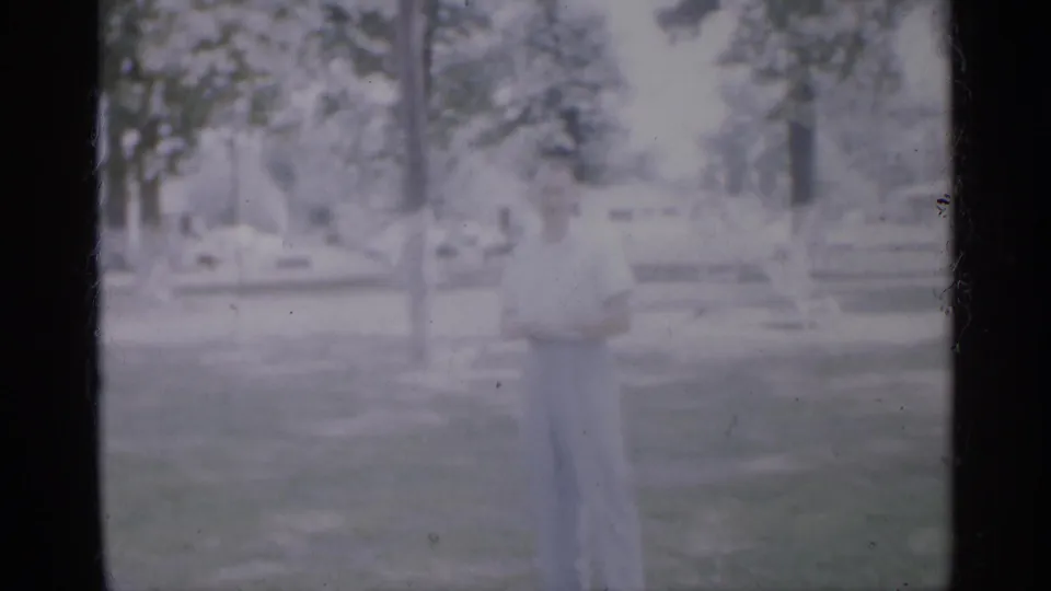 The man remains standing in grass, with trees and low park seating visible behind him in the faded 1958 New Jersey footage.