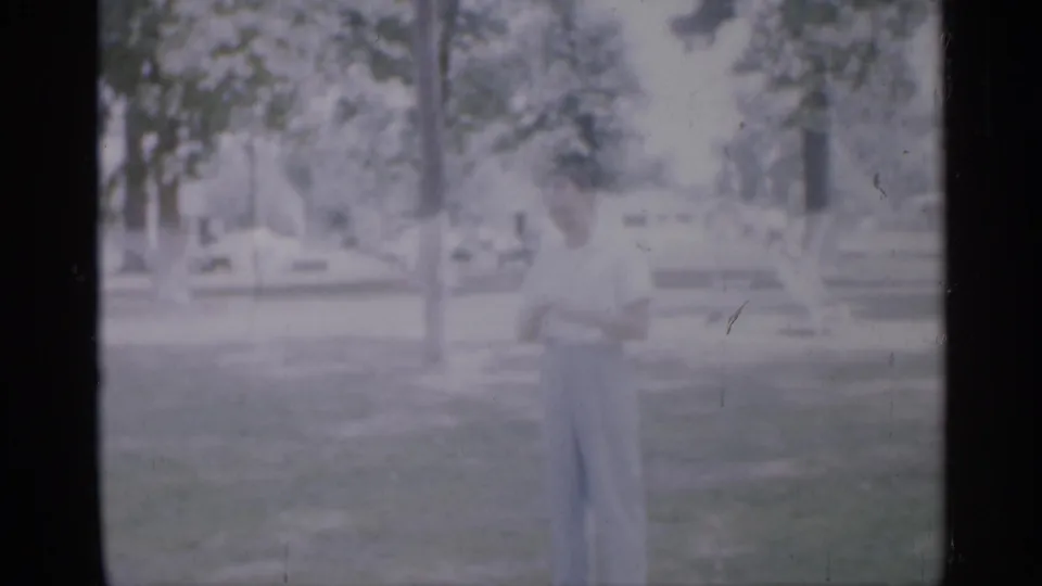 A soft, faded 8mm frame shows the man on grass, apparently engaged with someone off-camera in a New Jersey park setting.