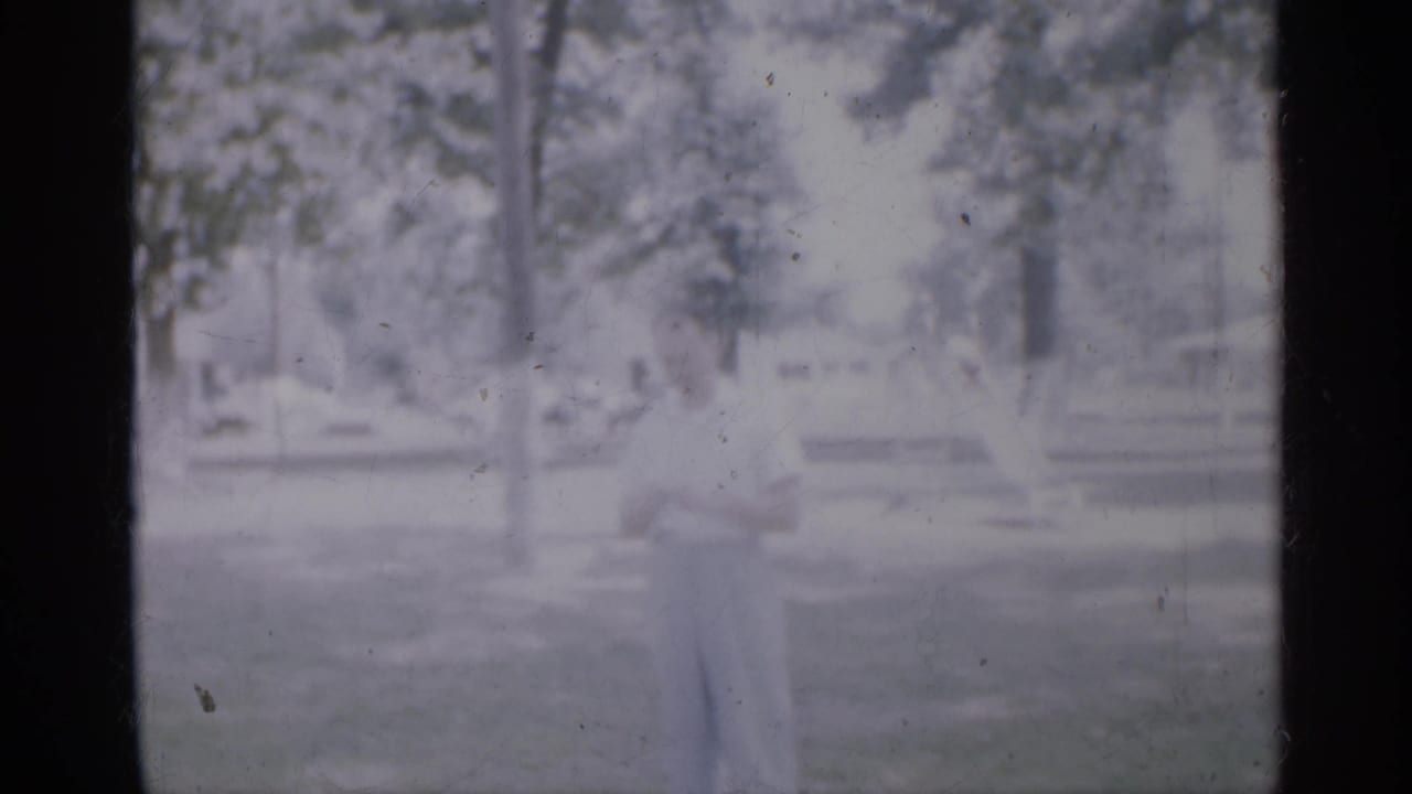Small child standing on grass in a bright park with trees and low fixtures behind.