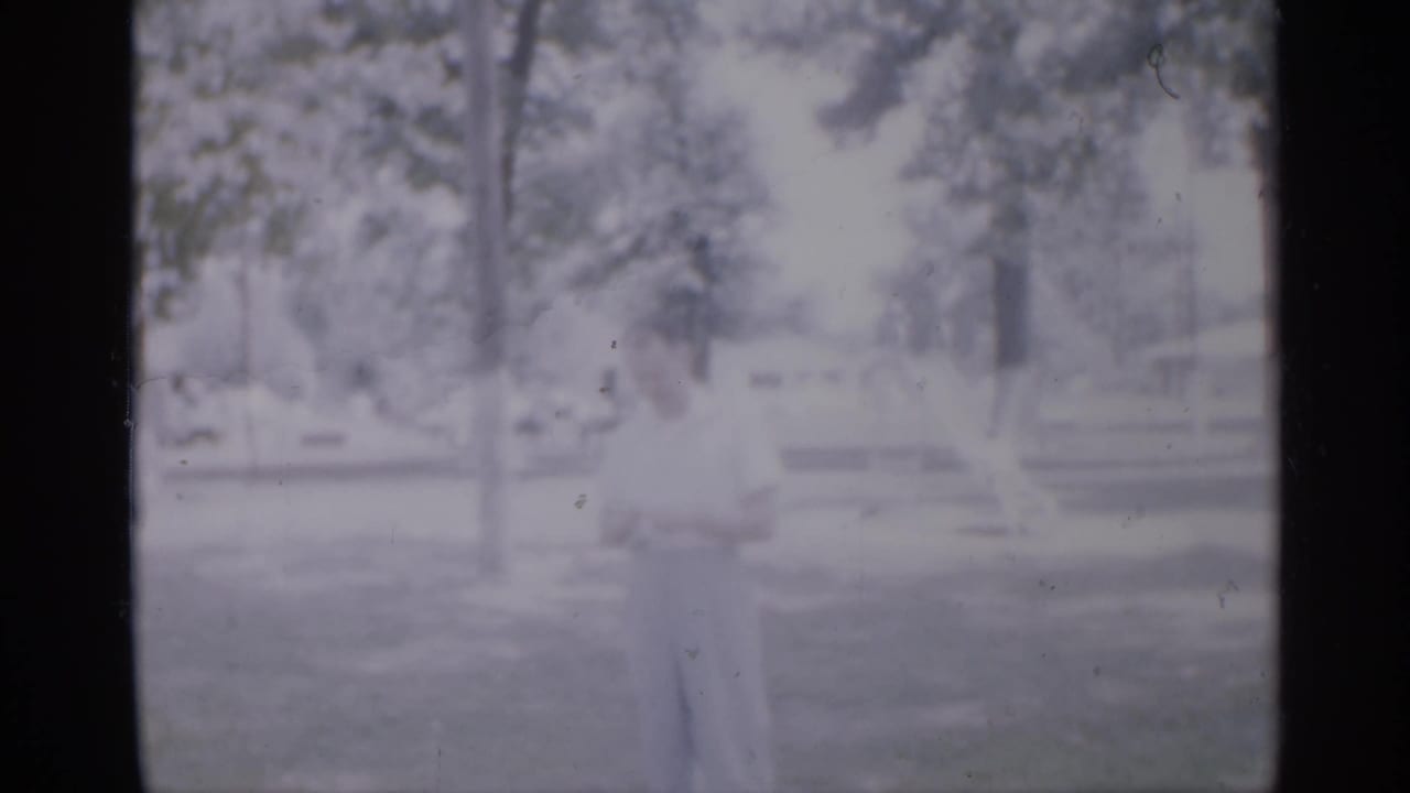 Child standing in a sunlit grassy area with trees and park structures in the distance.