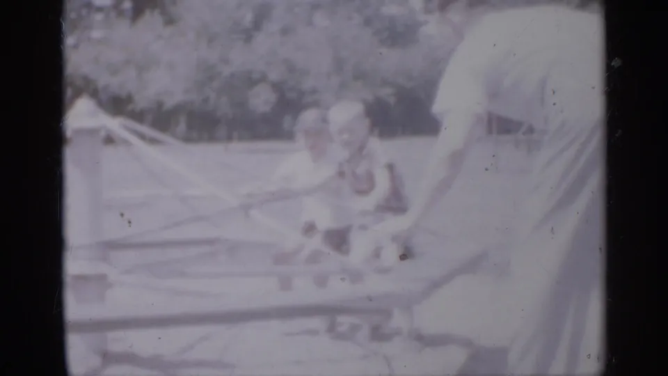 A child appears near low playground rails in a 1958 New Jersey home-movie frame, with another person partly visible at the right edge.