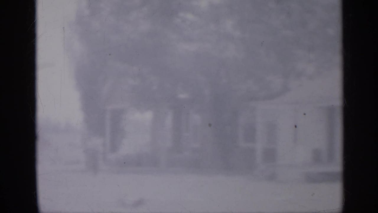 1958 New Jersey 8mm frame showing a soft, motion-blurred rural view through vehicle window dividers, with a faint house and trees beyond.