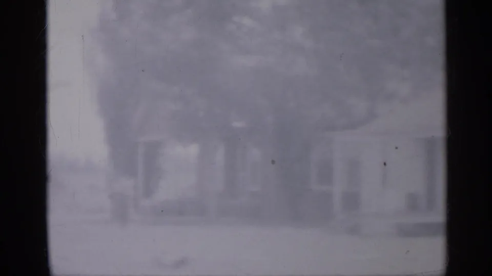 1958 New Jersey 8mm frame showing a soft, motion-blurred rural view through vehicle window dividers, with a faint house and trees beyond.