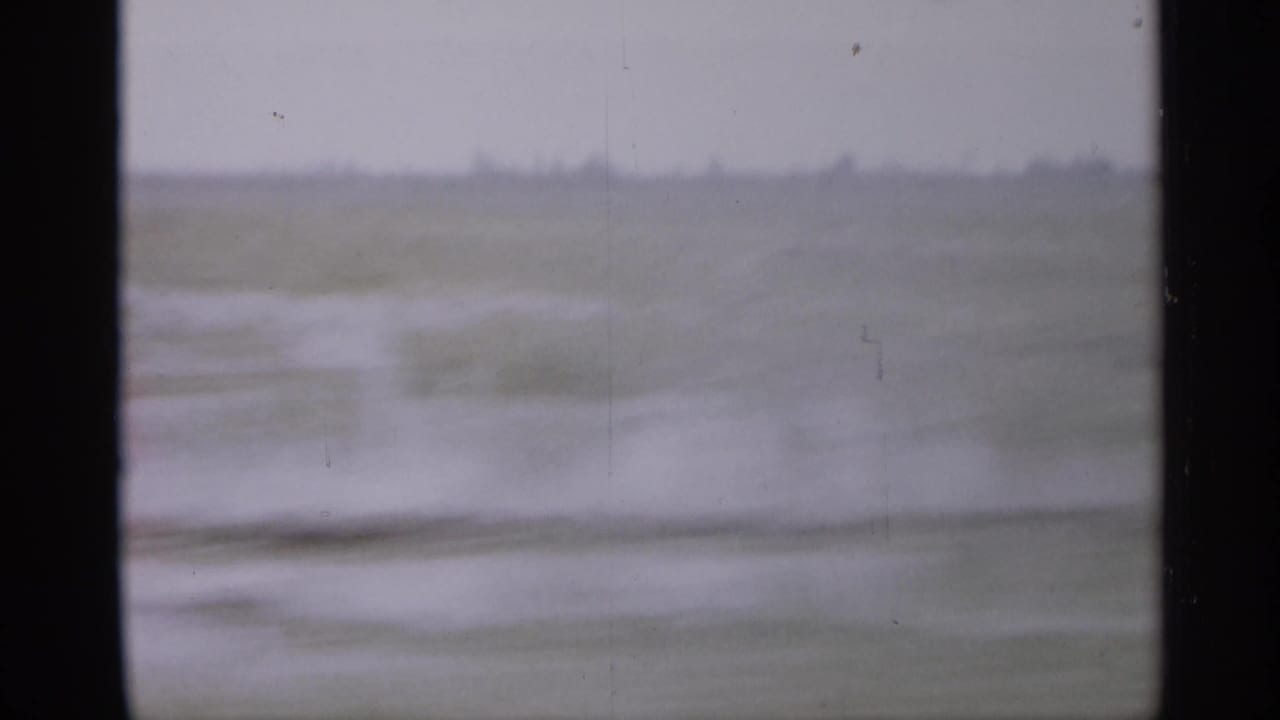 Blurred open landscape seen through a dark vehicle window frame.