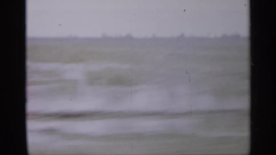 1958 New Jersey home-movie frame showing flat open land and a hazy horizon through a dark car window frame.
