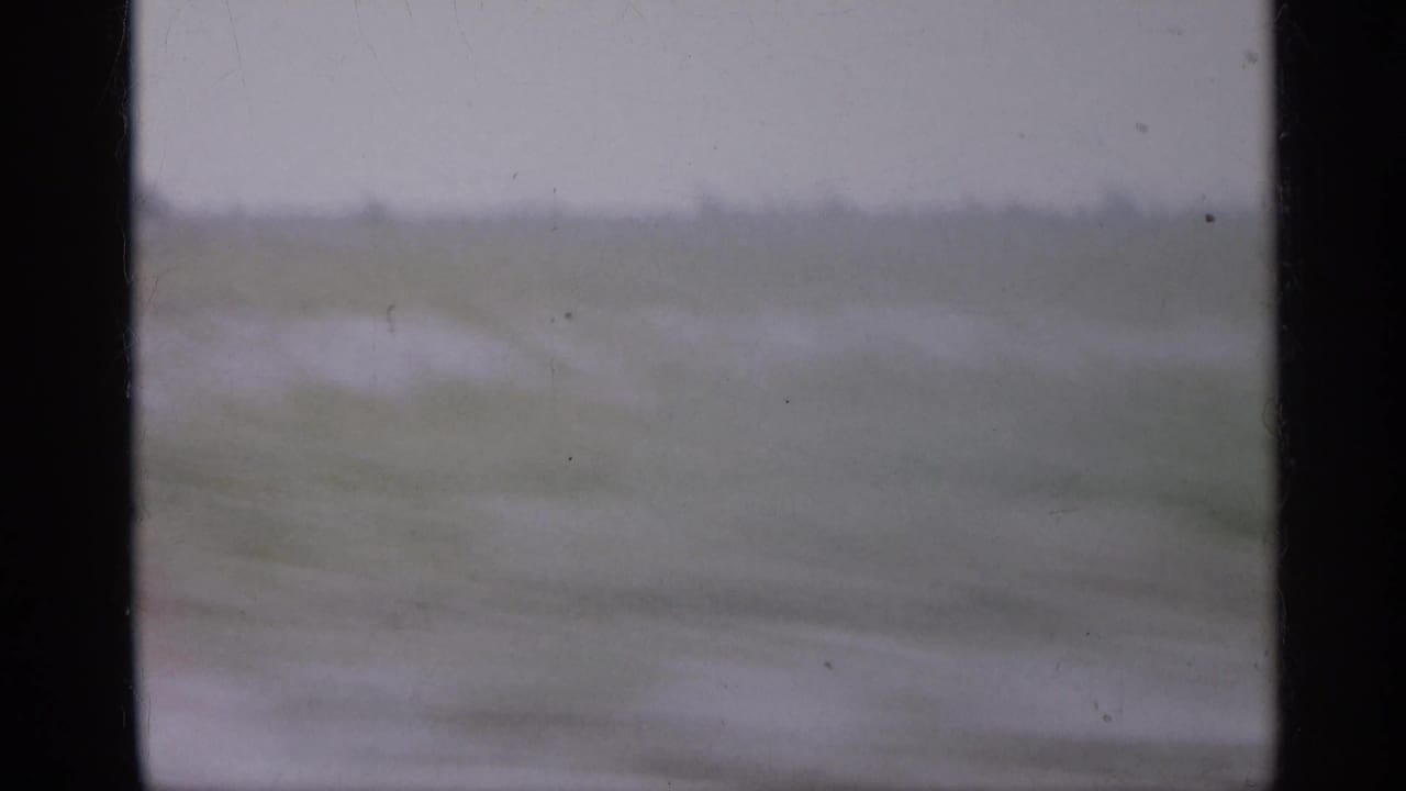 1958 New Jersey 8mm frame with muted fields, pale sky, and a dark interior window edge during rapid travel.