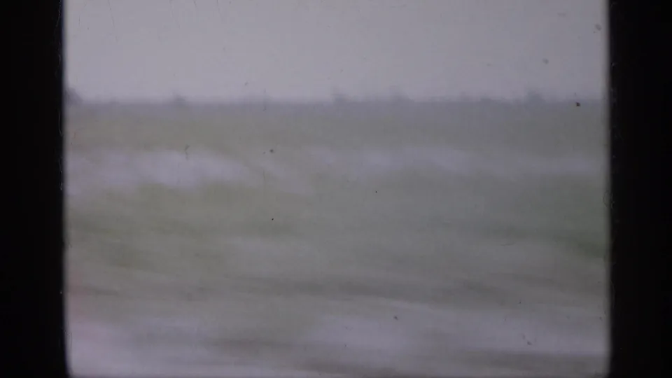 1958 New Jersey 8mm frame with muted fields, pale sky, and a dark interior window edge during rapid travel.