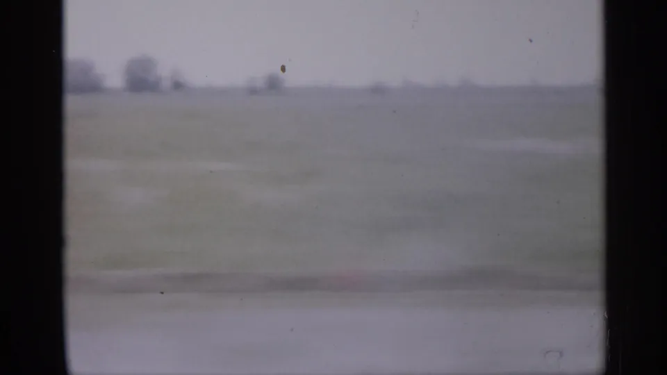 1958 New Jersey home-movie view of flat fields and distant trees framed by the dark edge of a moving vehicle window.