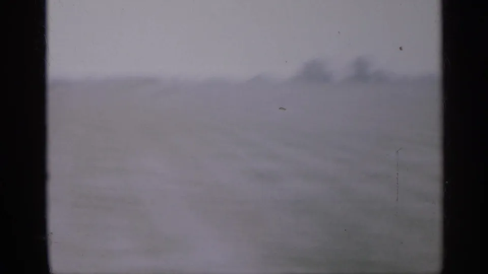 1958 New Jersey 8mm frame showing a blurred open lot or road edge under a pale overcast sky, bordered by dark film-frame edges.