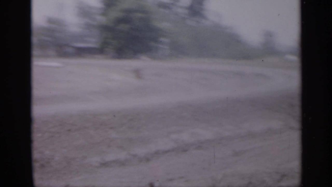 1958 New Jersey 8mm frame with a soft view across open ground toward a distant tree line and possible road surface.