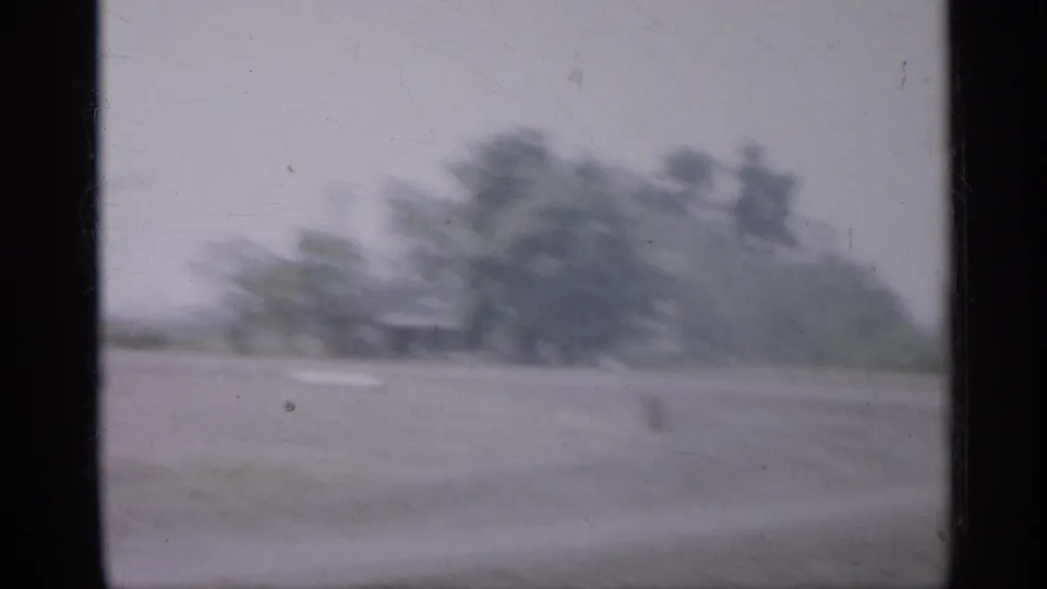 1958 New Jersey 8mm frame showing a flat open lot and blurred tree line, with muted color and visible film wear.