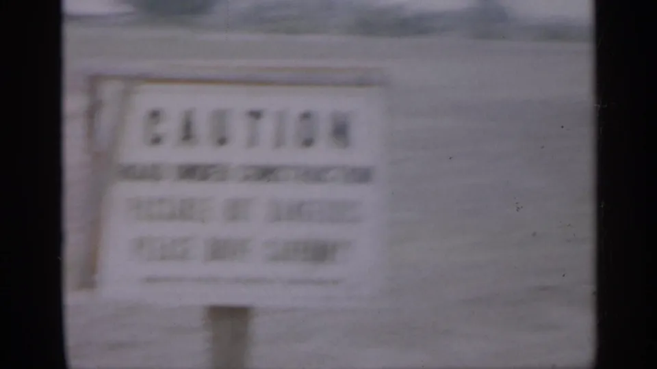 The caution sign fills more of the frame, still soft and partly unreadable, with grassy suburban background visible.