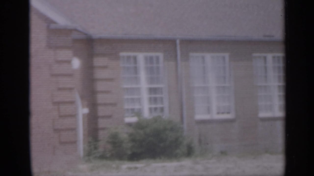 Blurred brick building facade with white windows seen through dark film gate edges.