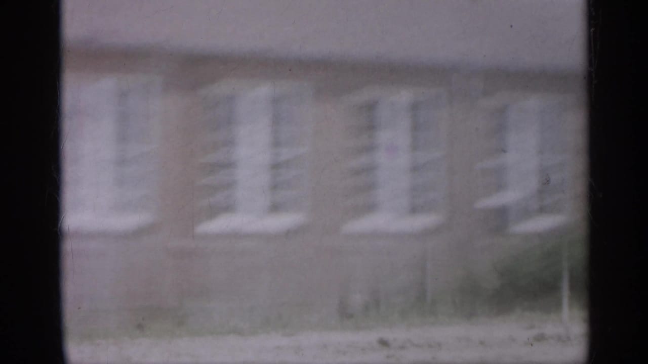 1958 New Jersey frame with a blurred brick facade and repeated white windows as the camera moves past.
