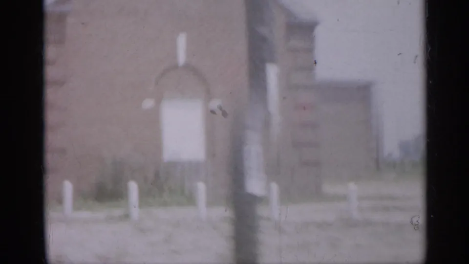 1958 New Jersey frame with a soft-focus brick exterior, a pale signboard or panel, roadside posts, and an adjacent roofline.