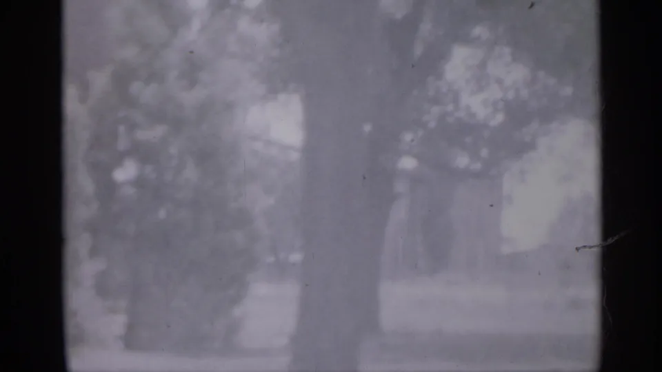 1958 New Jersey frame showing a flagpole, trees, and part of a school or civic building in soft focus.
