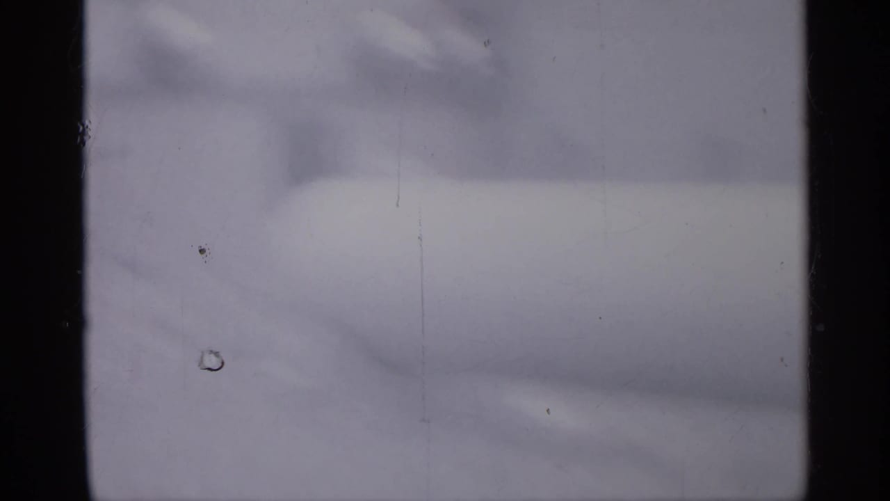 Blurred 1958 home-movie frame from New Jersey showing a large pale cylindrical tank shape near an exterior area, with heavy softness and film wear.