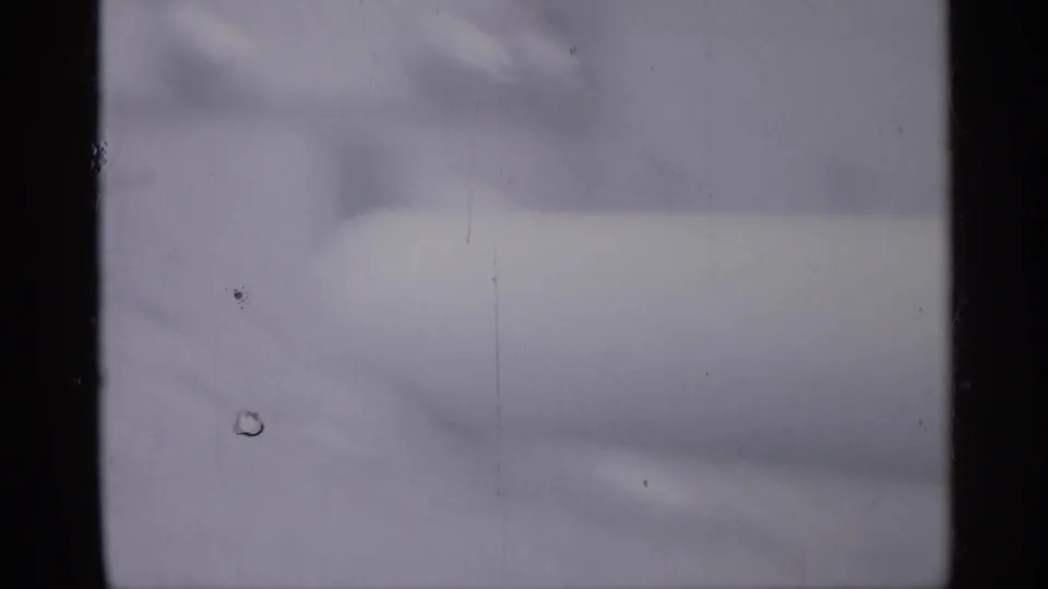 Blurred 1958 home-movie frame from New Jersey showing a large pale cylindrical tank shape near an exterior area, with heavy softness and film wear.