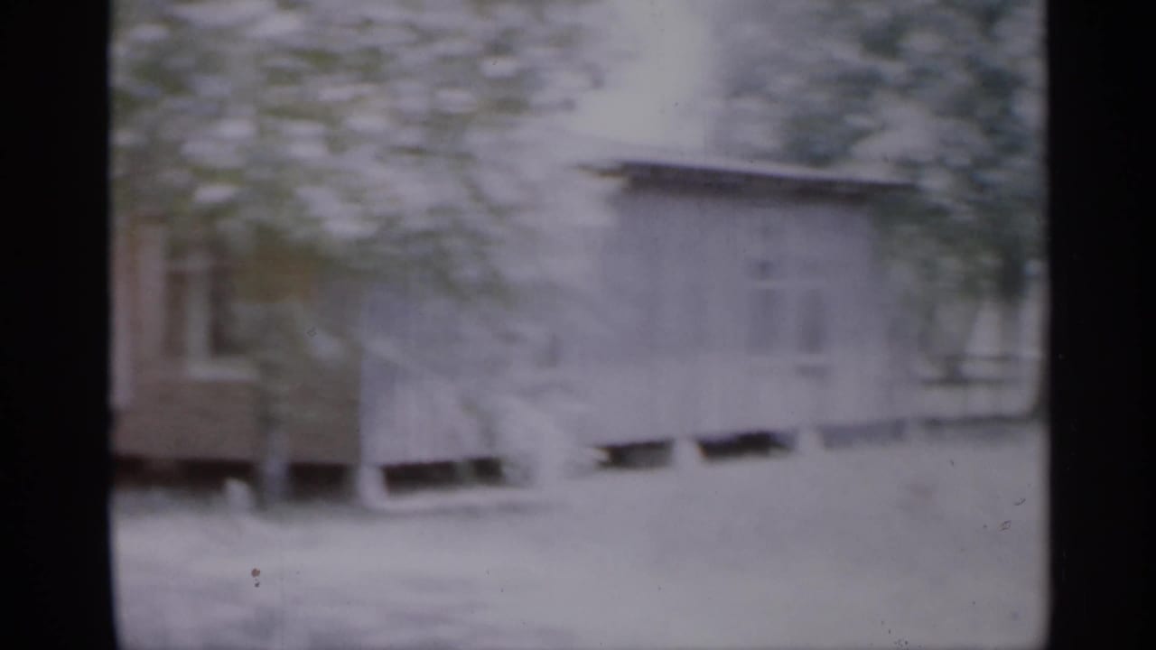1958 New Jersey frame with a brown house exterior, porch area, windows, and leafy branches in front.