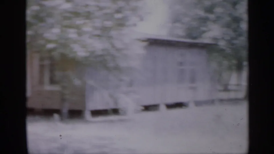 1958 New Jersey frame with a brown house exterior, porch area, windows, and leafy branches in front.