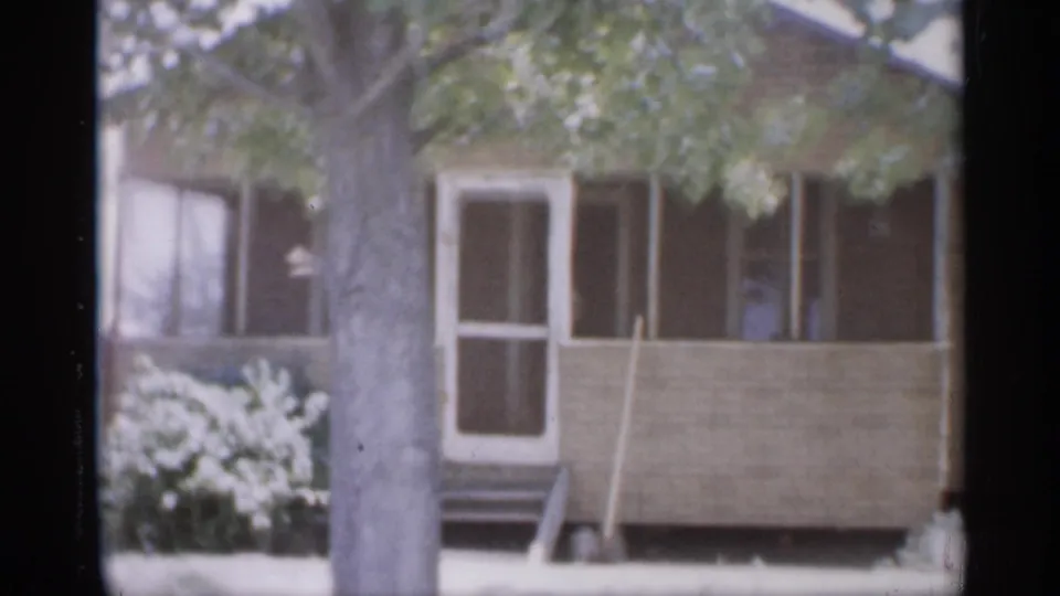 1958 New Jersey residential exterior showing a screened porch, white door, steps, shrubs, and a large tree trunk.