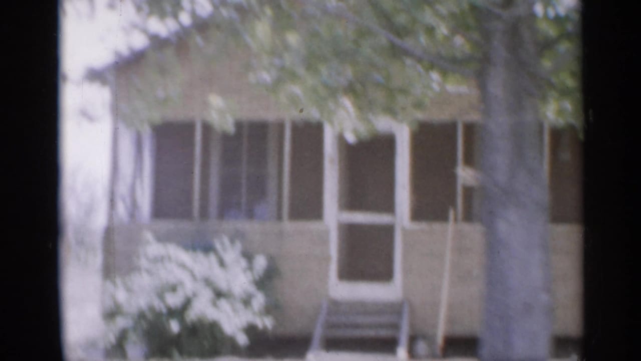1958 New Jersey 8mm frame showing a modest house exterior with porch, white trim, front steps, tree trunk, and shrubbery.