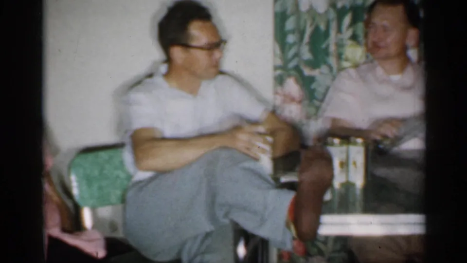 1958 New Jersey home-movie frame showing two men seated at a kitchen table during a casual indoor gathering.