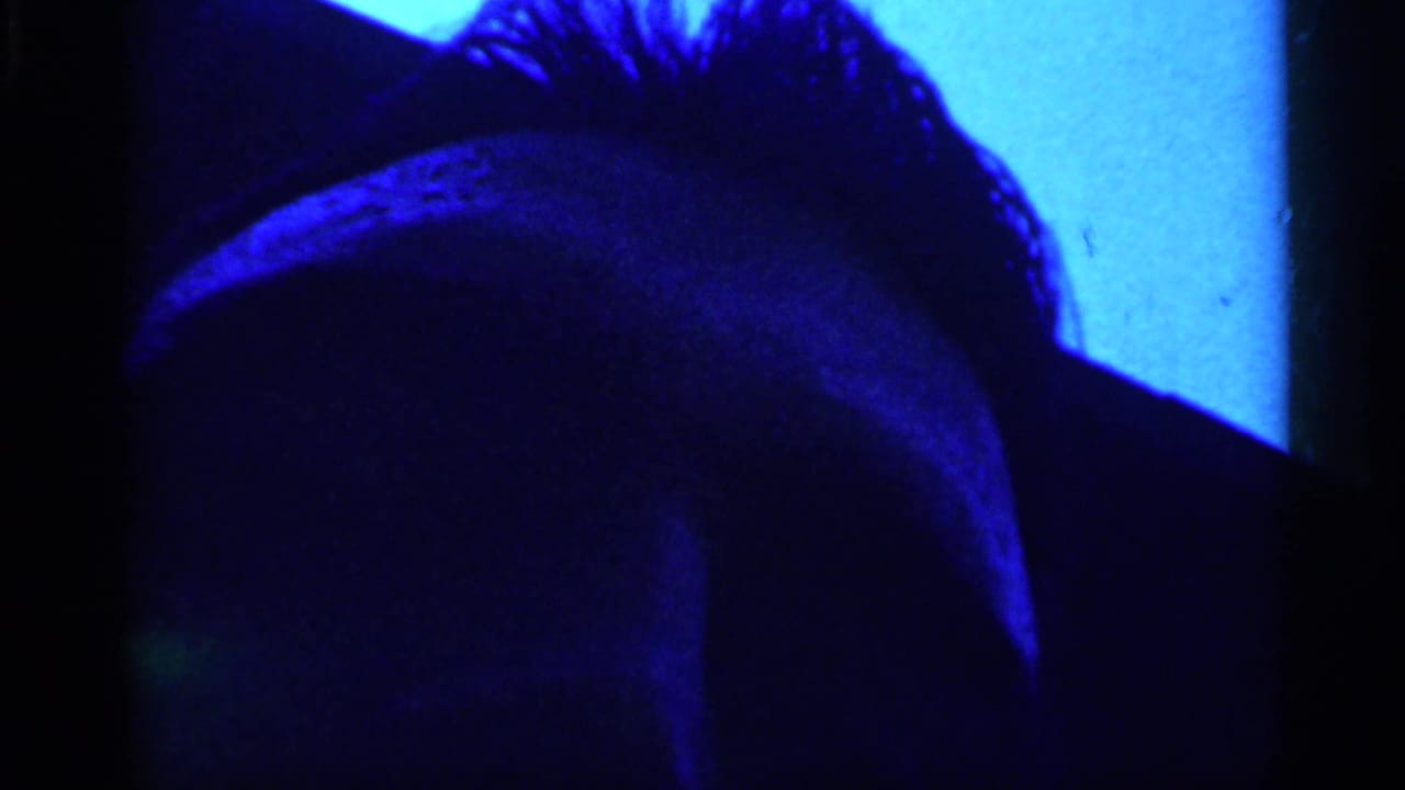 Blue-lit close-up of a shadowed person's head near a dark vertical edge.