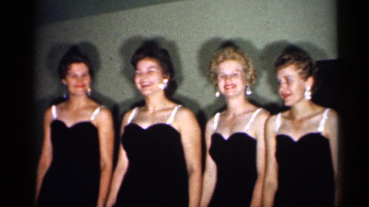1958 New Jersey 8mm frame showing four young women in formal dark dresses smiling for the camera.