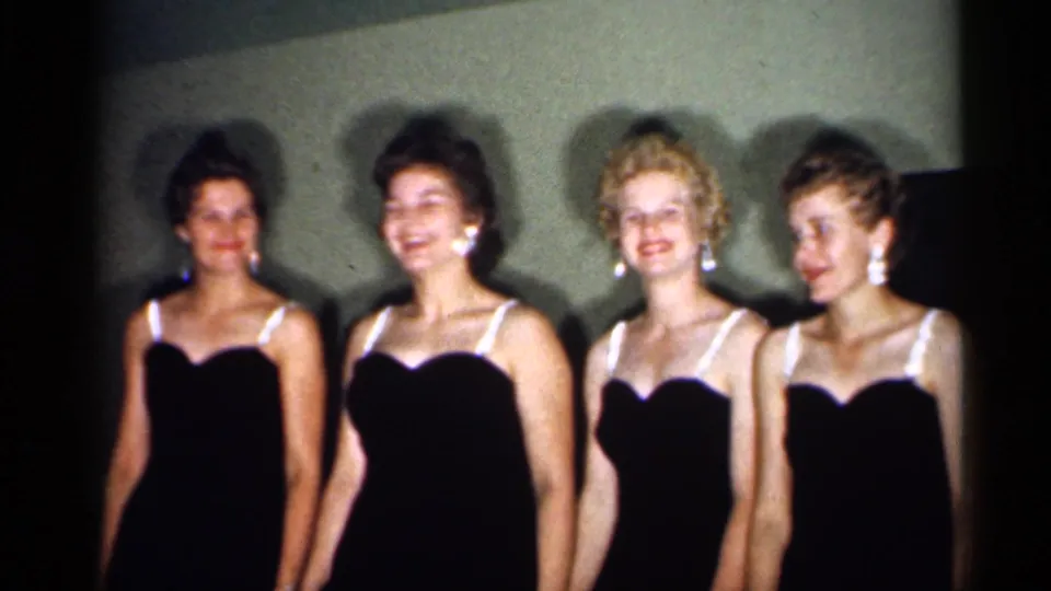 1958 New Jersey 8mm frame showing four young women in formal dark dresses smiling for the camera.