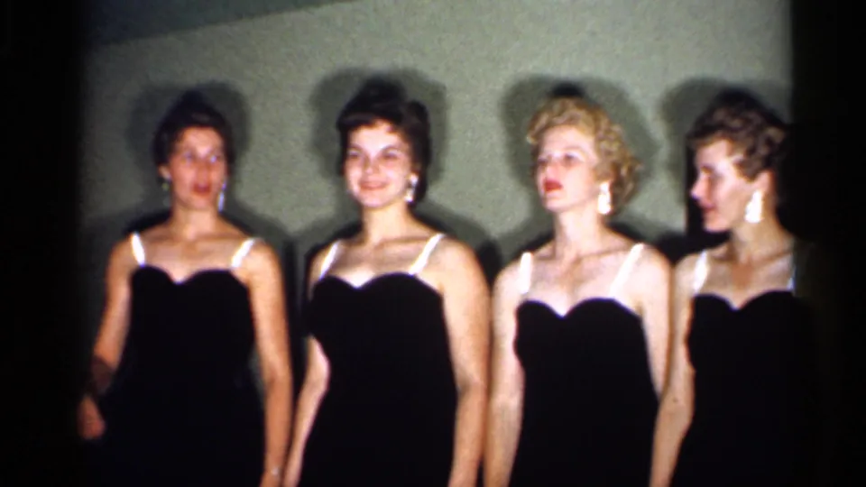 Four adult women in coordinated black dresses stand close together, with one looking sideways in the 1958 New Jersey clip.