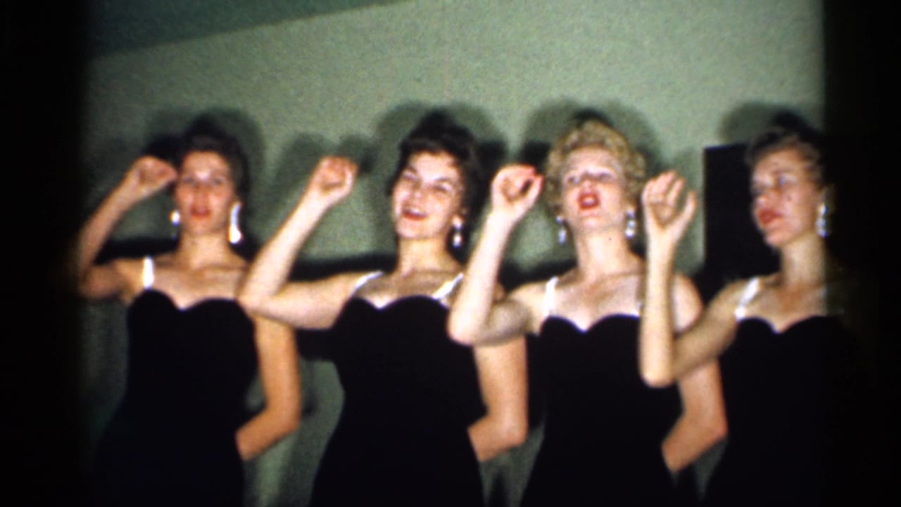 Four women in black formal dresses raise their hands together during a staged 1958 New Jersey home-movie performance.