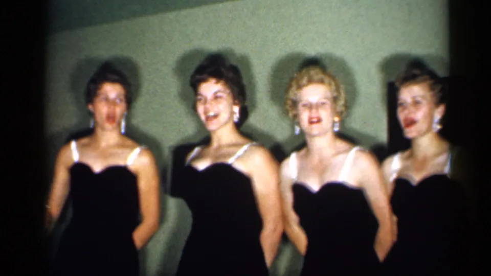 Four young women in black evening gowns pose indoors in 1958 New Jersey home-movie footage.