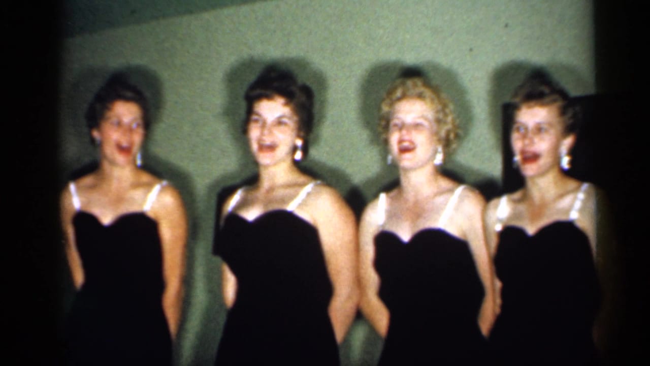 Four young women in formal black dresses face the camera during an indoor 1958 New Jersey performance.