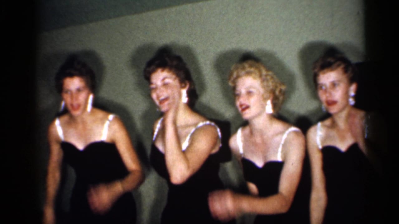 In 1958 New Jersey home-movie footage, four women in matching dark dresses with white straps appear to sing or dance against a plain wall.